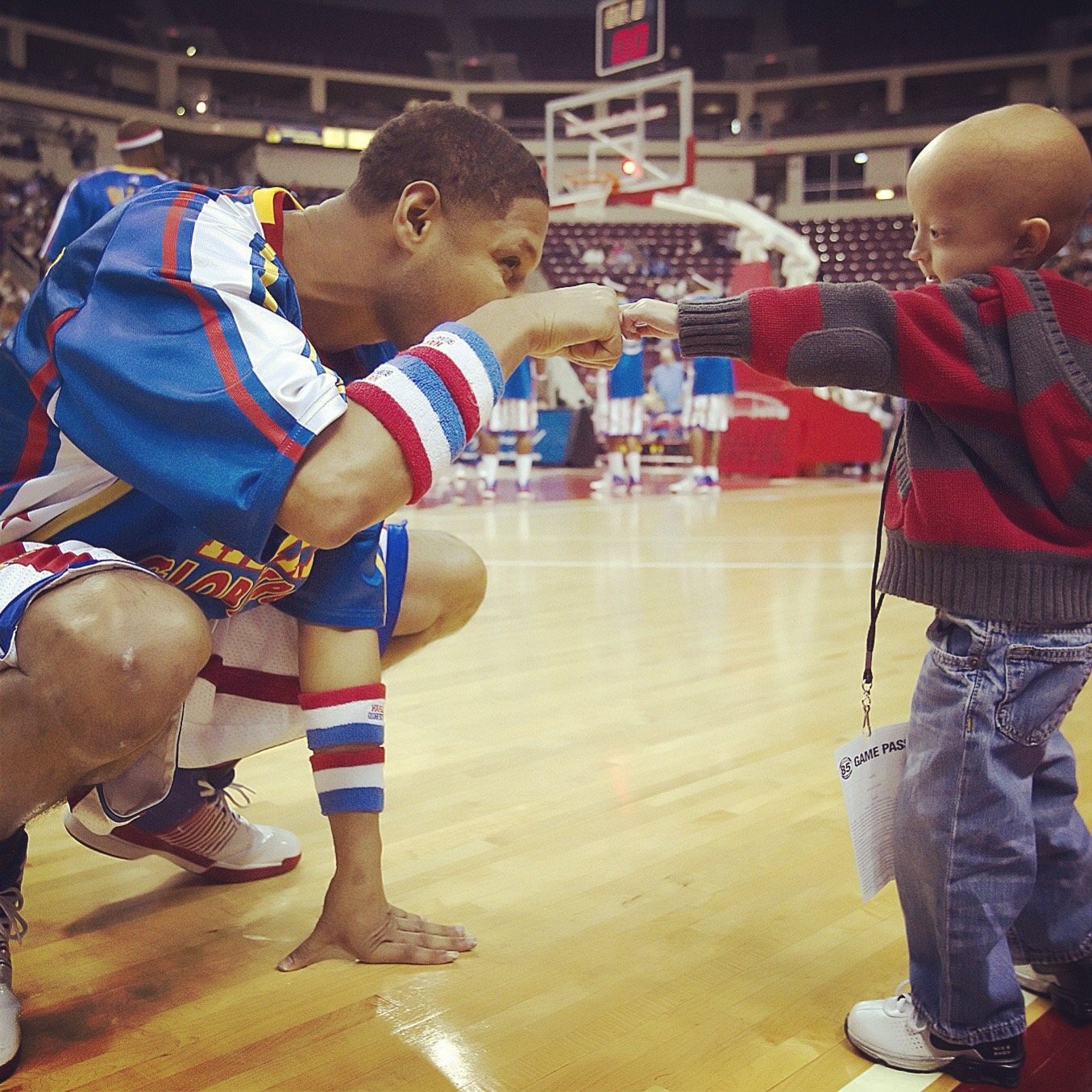 Chris “Handles” Franklin in Harlem Globetrotters uniform crouching to fist-bump a small child courtside
